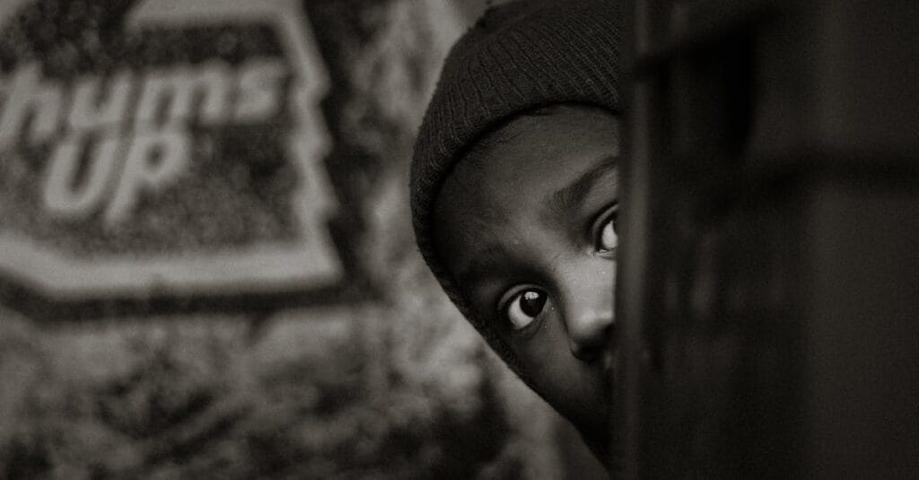 A captivating black and white portrait of a child peeking with curiosity and shyness.