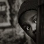 A captivating black and white portrait of a child peeking with curiosity and shyness.