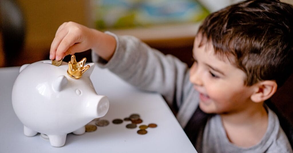 Young boy smiling while saving money in a crowned piggy bank, demonstrating financial responsibility.