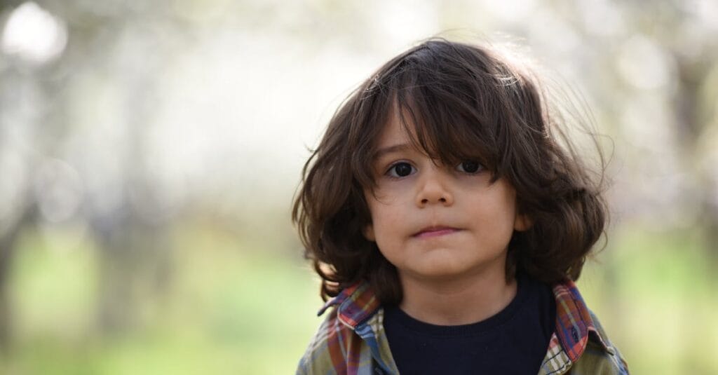 Portrait of a cute child with long hair wearing a plaid shirt, standing outdoors during spring.