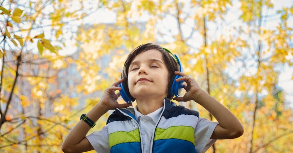 A young boy enjoys music through headphones amidst colorful fall foliage.