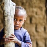 Portrait of a shy child peering behind a tree in Dodoma, Tanzania.