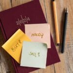 2024 planner with 'buy', 'hold', 'sell' notes and pens on a rustic wooden surface.