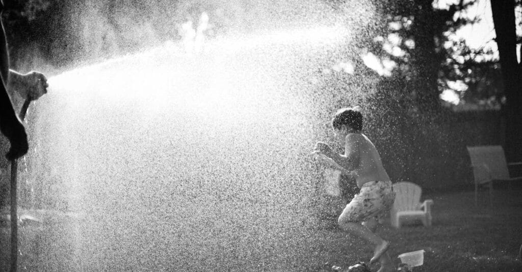 A child joyfully plays in water spray in a backyard, capturing summer fun.