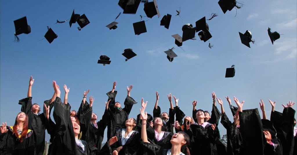 Group of graduates celebrating by throwing caps in the air during a sunny day.