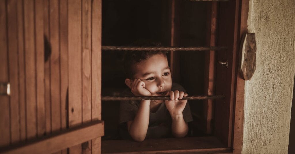 A thoughtful child rests at a window, gazing outside, conveying a moment of contemplation.