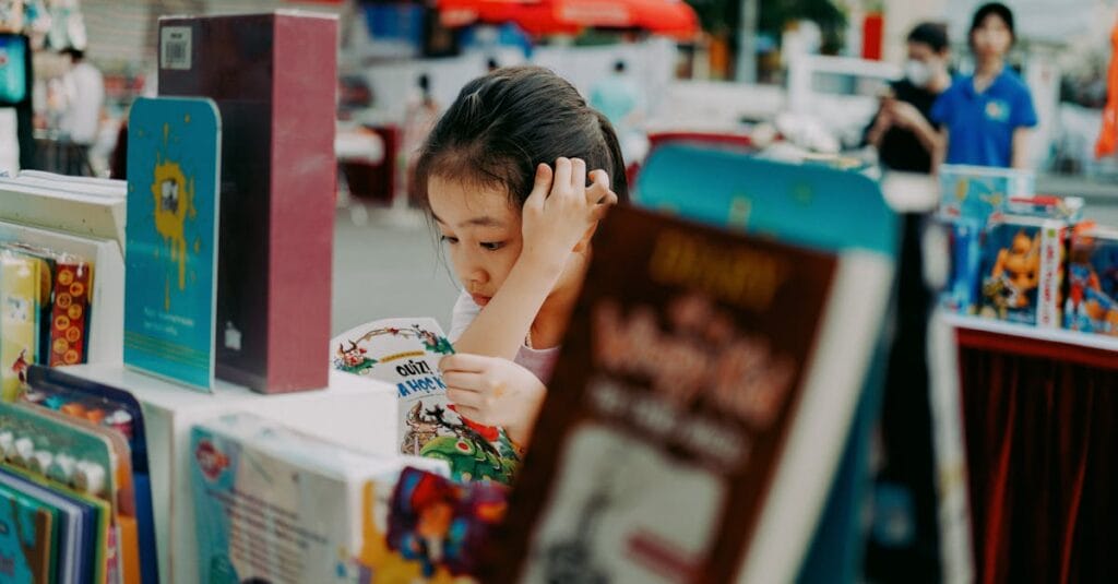 A young girl engrossed in a book at an outdoor book fair surrounded by colorful books and vibrant atmosphere.