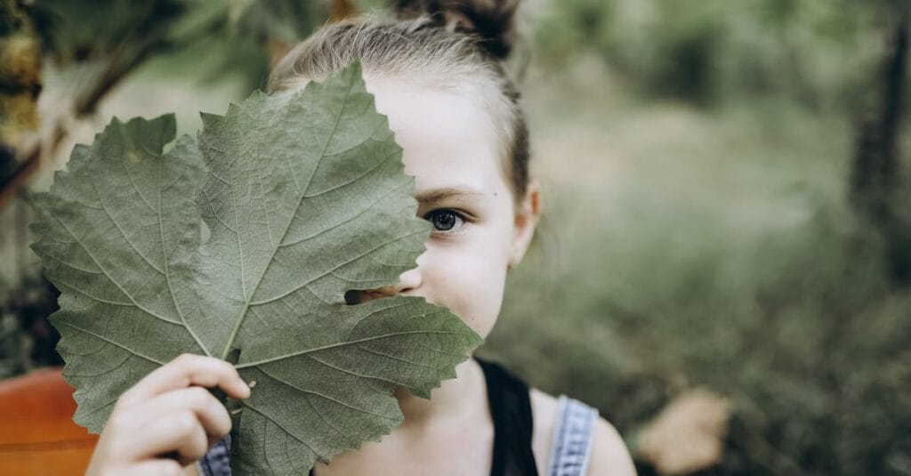 A charming young girl playfully holding a leaf in an outdoor setting, showcasing innocence.