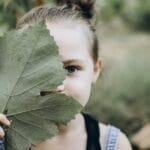 A charming young girl playfully holding a leaf in an outdoor setting, showcasing innocence.