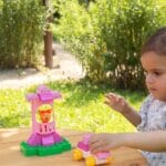 Adorable young girl playing with colorful toy blocks on a sunny day in the park.