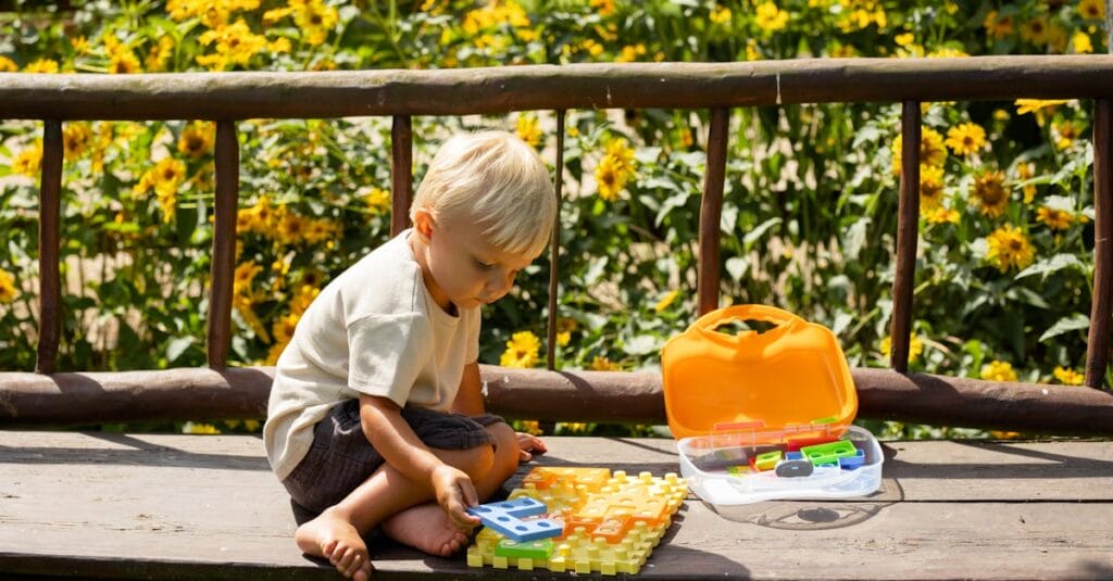A young boy playing with a colorful puzzle outdoors on a sunny summer day.