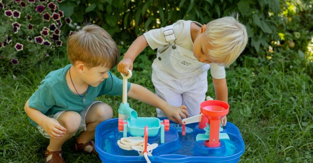 Two boys enjoying playing with a water toy outdoors during summer in a garden setting.