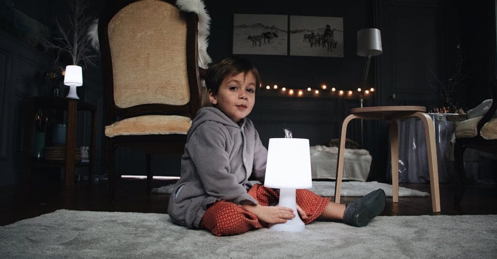 A young child sitting indoors next to a glowing lamp, creating a warm and cozy atmosphere.