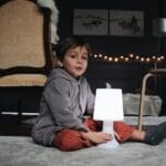 A young child sitting indoors next to a glowing lamp, creating a warm and cozy atmosphere.