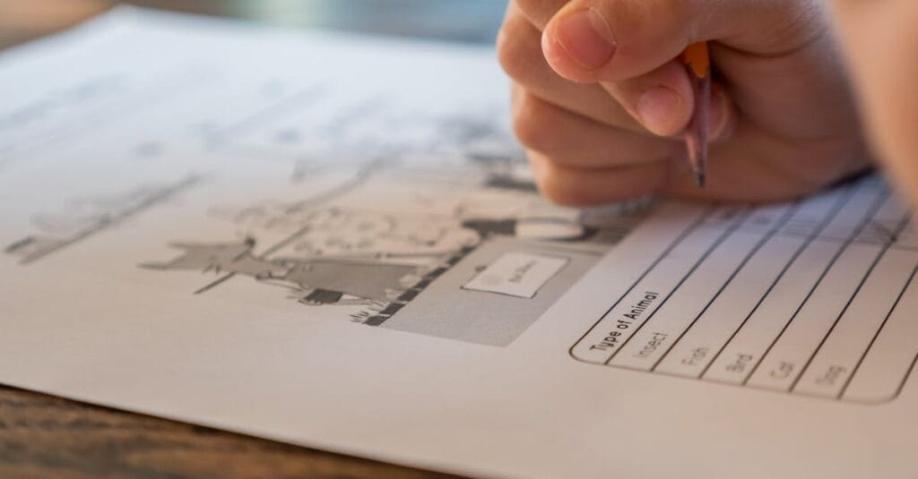 Closeup of crop anonymous elementary school pupil with pencil in hand doing marks on paper sheet with test about animals during lesson