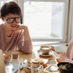 Two friends sharing breakfast and coffee at a cozy cafe, relaxed and happy.