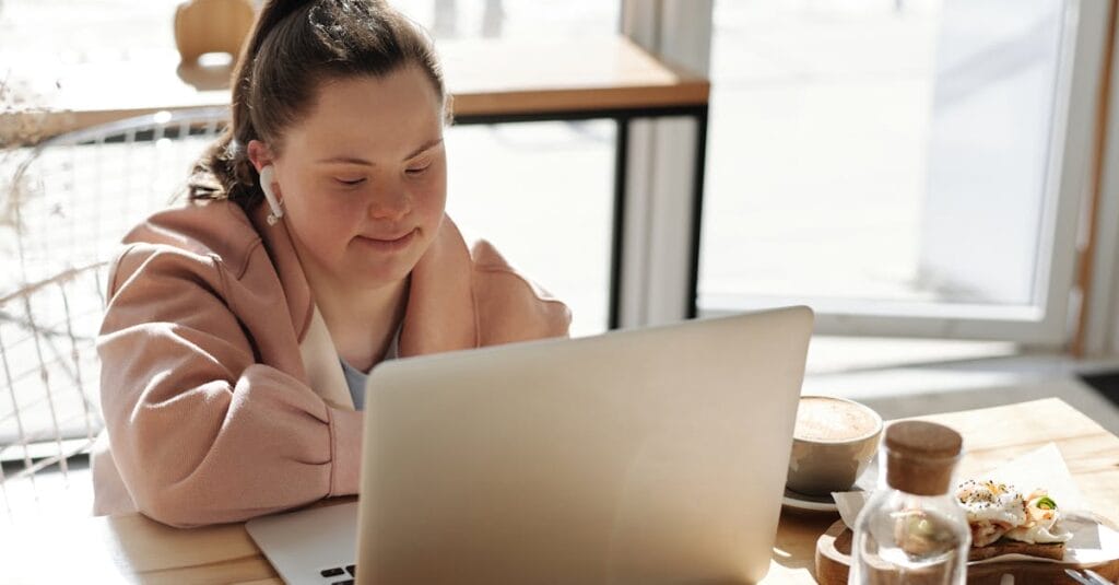 Young woman with Down syndrome using a laptop at home, enjoying coffee. Perfect for lifestyle and technology themes.