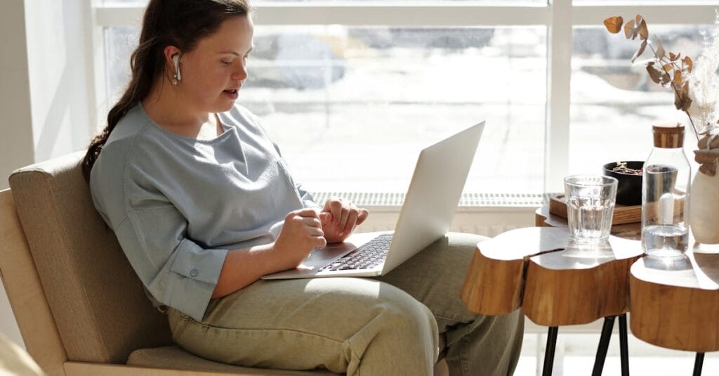 Young woman with Down syndrome using a laptop at home in a bright, cozy space.