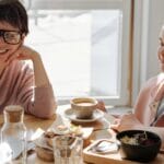 Two cheerful women enjoying coffee and food in a bright, modern indoor setting.