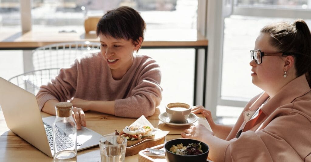 Two women enjoying coffee and conversation while working on a laptop in a relaxed café.