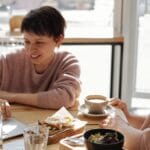 Two women enjoying coffee and conversation while working on a laptop in a relaxed café.