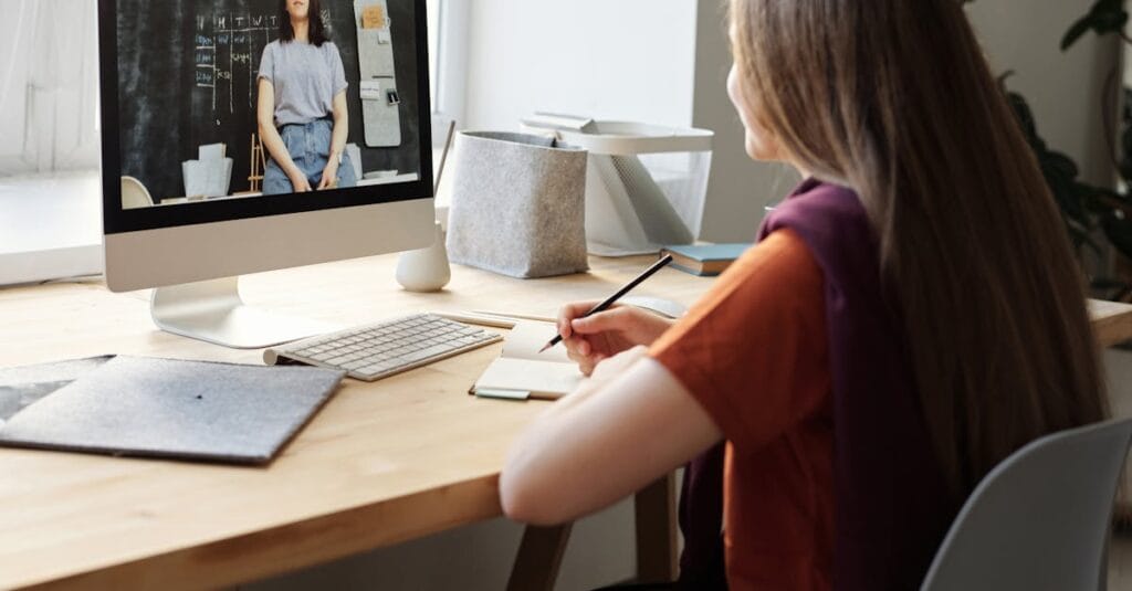 Teen girl attending an online class at home, takes notes at her desk.
