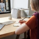Teen girl attending an online class at home, takes notes at her desk.