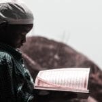 A young boy reading the Quran outdoors in Abuja, Nigeria, symbolizing faith and learning.
