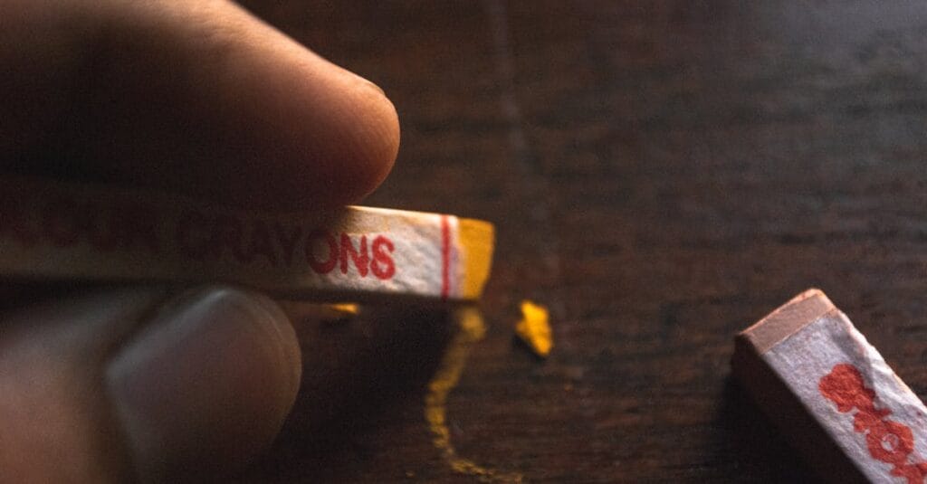 Detailed close-up of fingers holding a crayon drawing on a wooden surface.