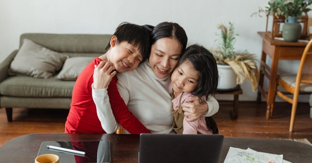 A mother embraces her children while working from home, blending family time with remote work.