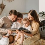A joyful family shares a book indoors, surrounded by houseplants, promoting reading and togetherness.