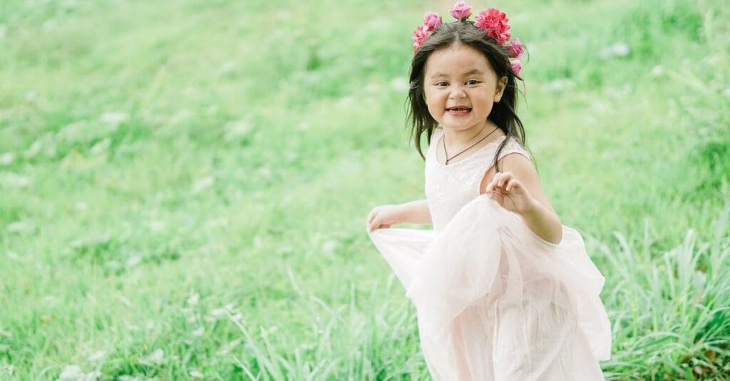 A joyful young girl wearing a floral crown runs playfully through a green park.