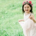 A joyful young girl wearing a floral crown runs playfully through a green park.