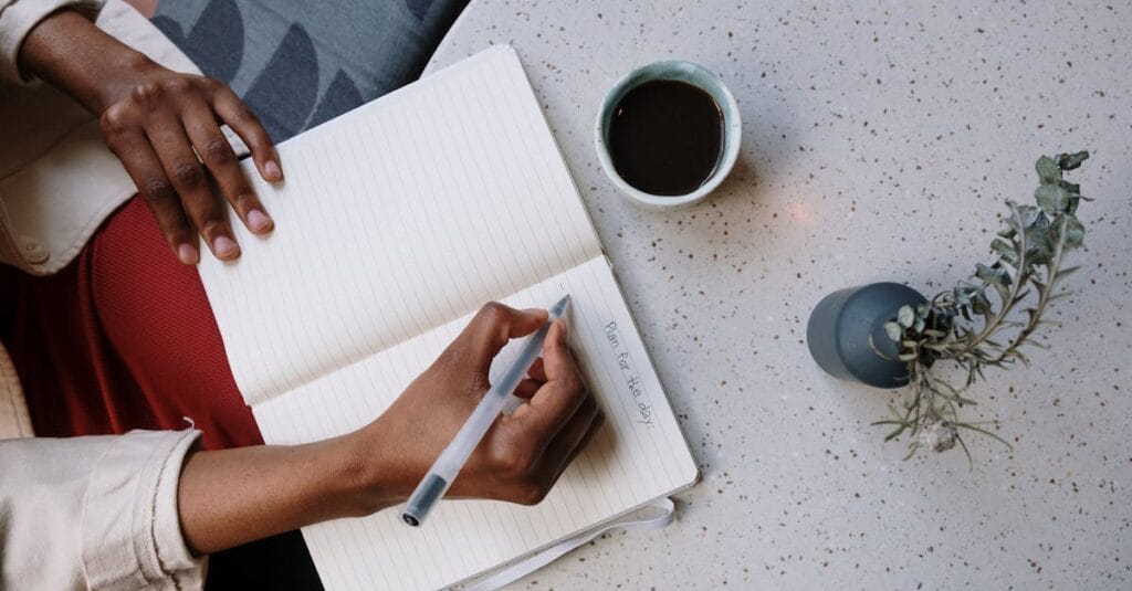 Person writing in a planner with coffee at a café, focusing on planning and productivity.