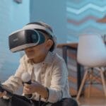 A young boy seated indoors, enjoying an immersive virtual reality gaming experience with VR goggles and controllers.
