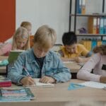 A group of children studiously engaged in writing and learning in a vibrant classroom setting.