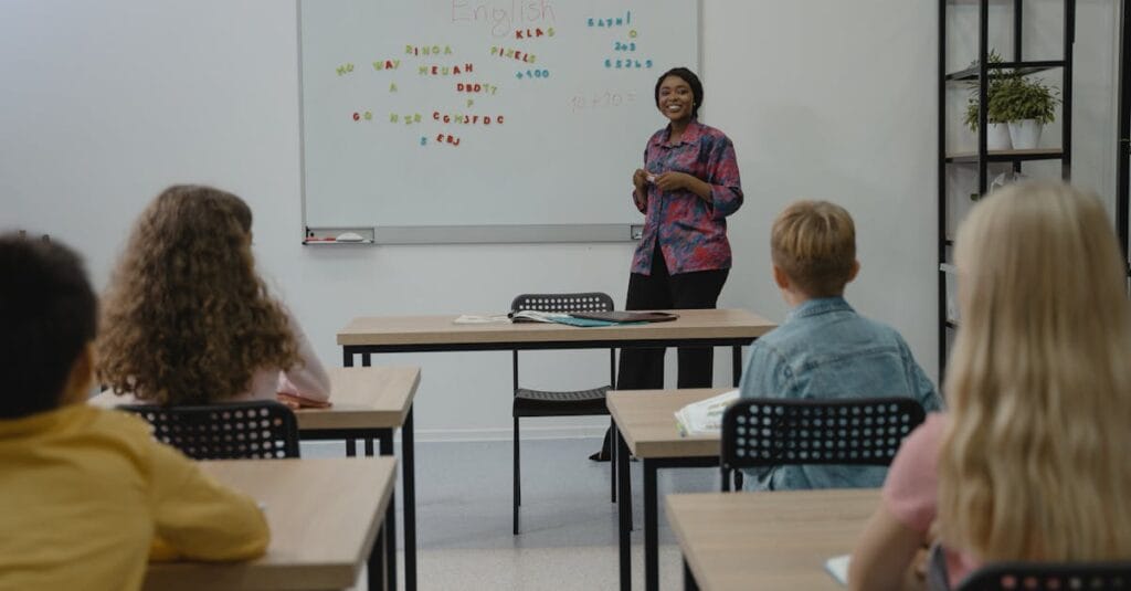 A diverse group of students in an English class with a smiling teacher at the whiteboard.