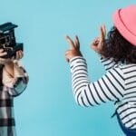 Two children in playful poses indoors capturing moments with a vintage camera.