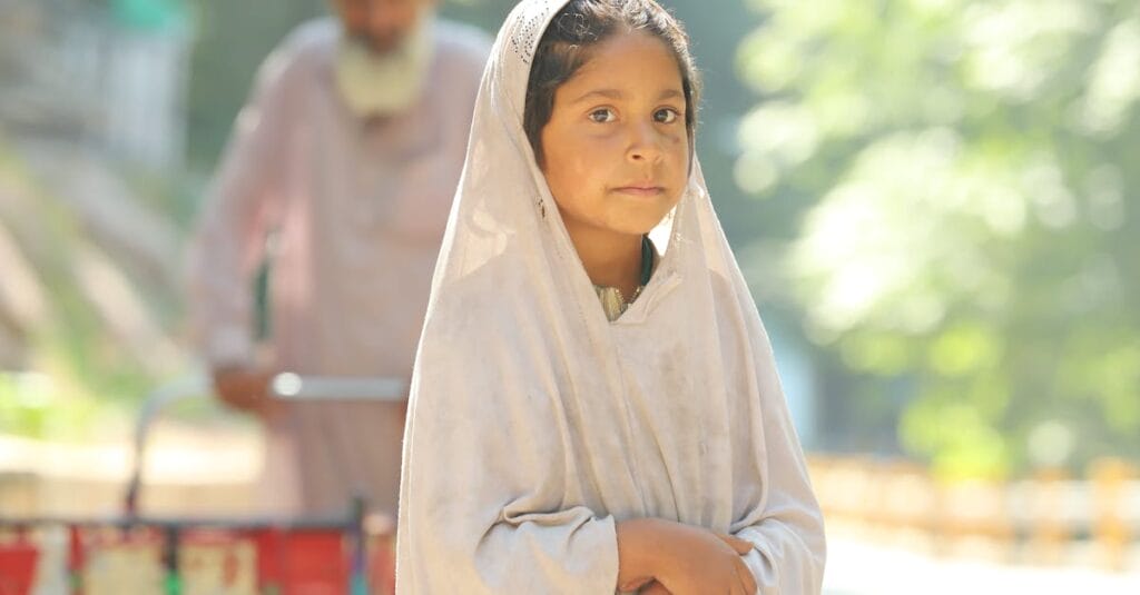 A young girl stands outdoors, looking at the camera with a serene expression in traditional attire.