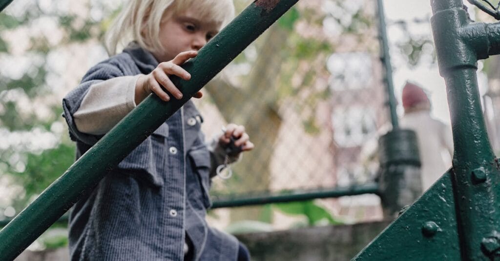 Blond child climbing a green metal staircase outdoors, showcasing carefree childhood curiosity.