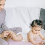 A loving mother gently massaging her baby's leg while the child plays indoors.