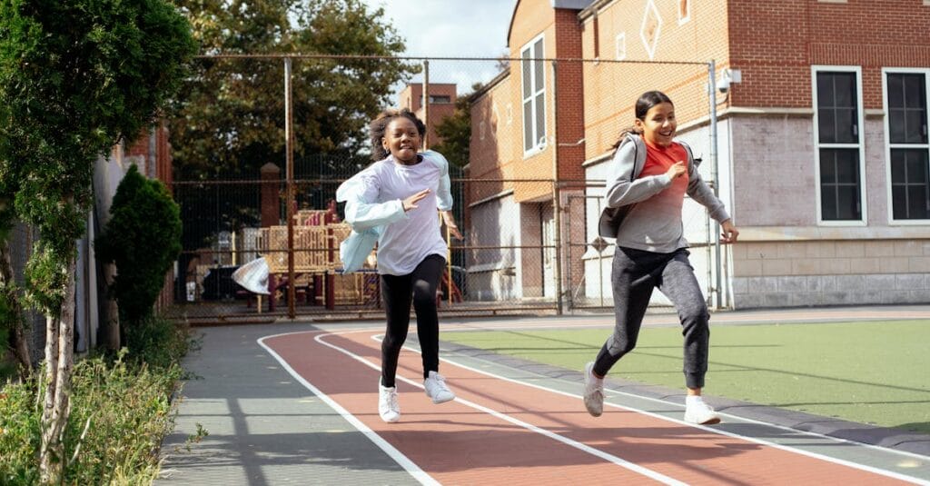 Full length of multiracial girls in sportswear and sneakers racing with each other on sports ground near school
