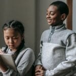 Two children engaged in a classroom activity, one smiling and the other taking notes.