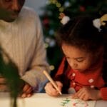 A father and daughter bond over drawing Christmas crafts indoors, capturing holiday spirit and family togetherness.