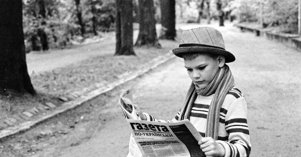Young boy in vintage attire reading a Ukrainian newspaper in a Lviv park.