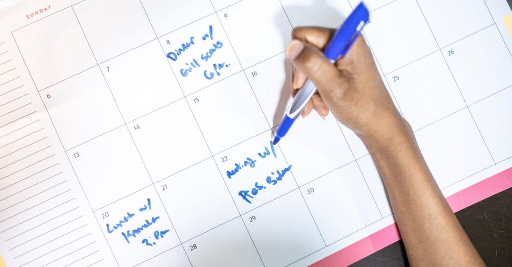 Person writing appointments on a calendar with a blue pen. High angle view.