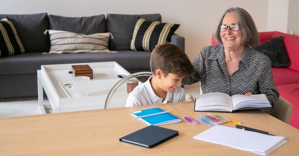 Happy grandmother assisting her grandson with homework indoors, creating a joyful learning atmosphere.