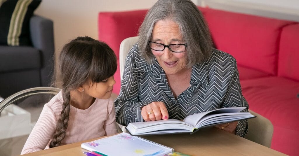 A joyful grandmother reading a book with her granddaughter indoors, bonding over learning.