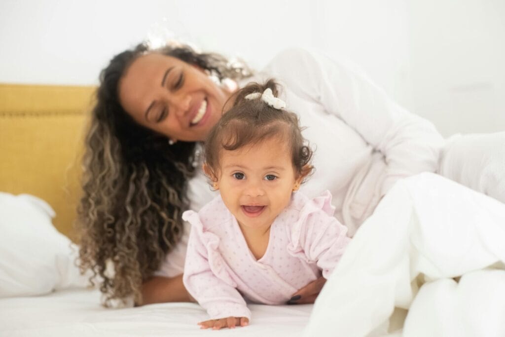 A joyful mother and baby daughter enjoy a loving moment on a comfy bed with natural light.