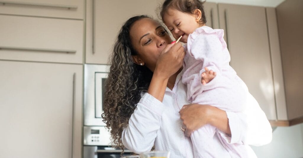A loving mother feeds her child in a warm kitchen, capturing a moment of tenderness and care.